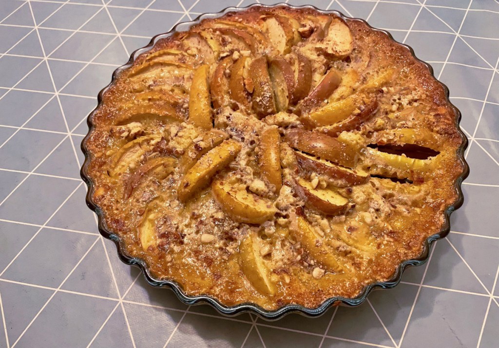 A round apple pie with large slices of apples and ground almonds on top.
