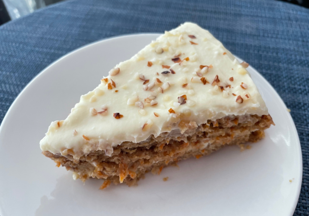 A slice of carrot cake with crushed hazelnuts sprinkled on top