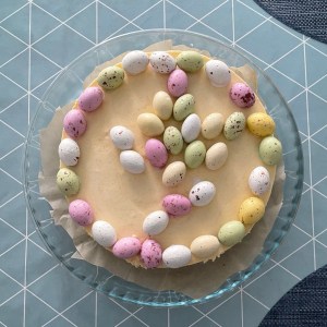 A light yellow cheesecake on a plate. The cake is decorated with small colourful egg-shaped candies.